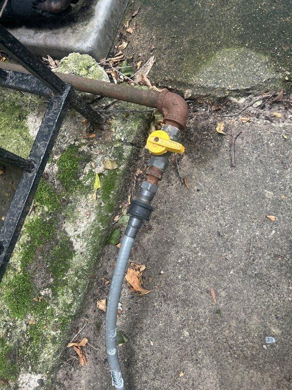 Completed assessment of exterior gas line serving outdoor grill. Found damaged flexible gas hose with evidence of animal chewing, creating potential safety hazard. Inspected existing gas line assembly including brass fittings, shut-off valve with yellow handle, and connection points. Documented corroded metal piping sections and transition to plastic piping at concrete pad location. Provided estimate for replacement of damaged gas line components to restore safe operation of outdoor grill connection.