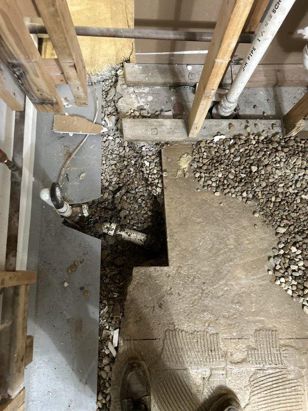 Completed rough-in plumbing installation in basement construction area, including placement and securing of white PVC drainage piping per ASTM D2665 specifications. Coordinated pipe routing through floor joists alongside existing HVAC ductwork, excavated and prepared foundation openings for proper drainage connections, and backfilled with gravel aggregate to ensure stable substrate for piping system.