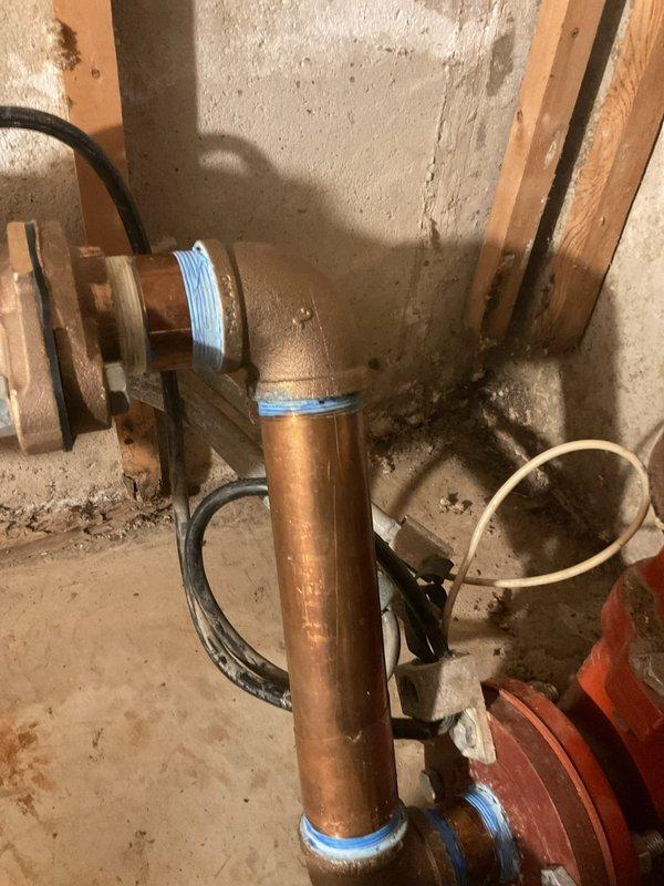 Responded to a recurring water leak in the basement plumbing system. Performed leak location assessment on copper piping with brass fittings and identified the source at a 2" brass 90-degree elbow connection. Marked affected areas with blue tape for reference and documented the system configuration with photographs. Scheduled return visit to replace the defective 2" brass 90-degree fitting to resolve the ongoing leak issue.