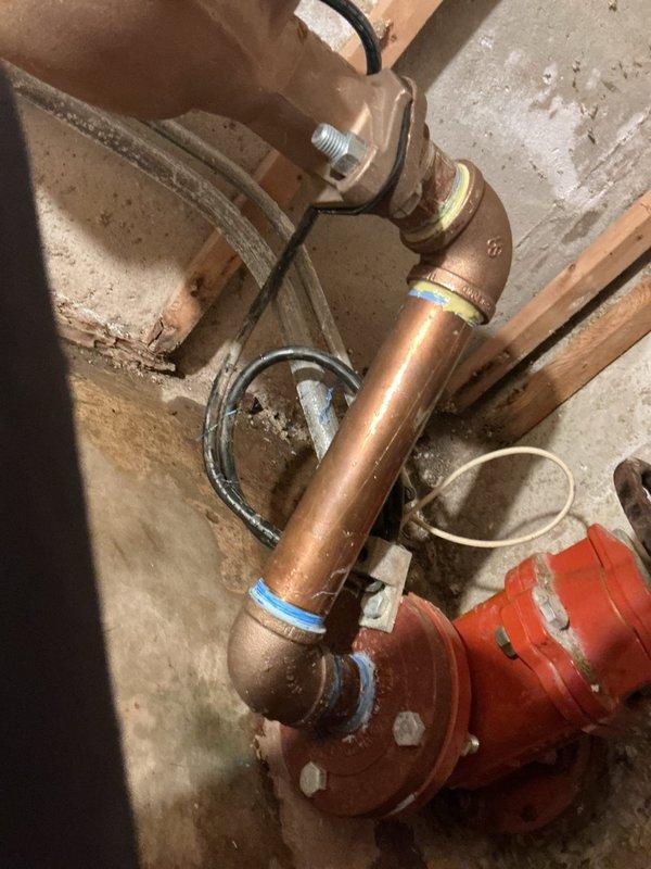 Responded to a recurring water leak in the basement plumbing system. Performed leak location assessment on copper piping with brass fittings and identified the source at a 2" brass 90-degree elbow connection. Marked affected areas with blue tape for reference and documented the system configuration with photographs. Scheduled return visit to replace the defective 2" brass 90-degree fitting to resolve the ongoing leak issue.