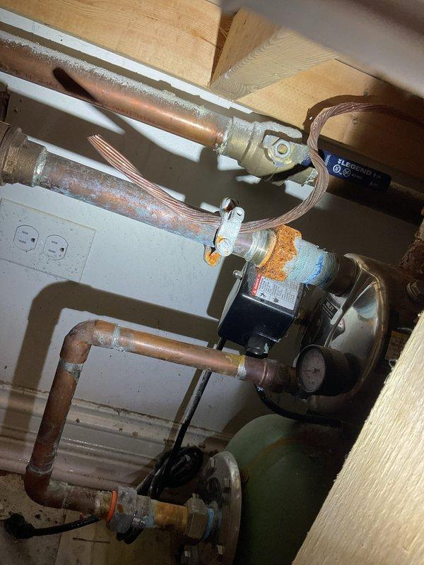 Completed comprehensive drain and sewer system evaluation for commercial property, documenting existing hydronic heating circulation system with copper piping infrastructure and mechanical pump assembly, as well as compressed air system with associated plumbing connections. Photographed current equipment conditions including circulator pump, copper supply and return lines, pressure tank compressor unit, and various valve assemblies to provide detailed assessment for proposed drainage and sewer line modifications in the utility area.