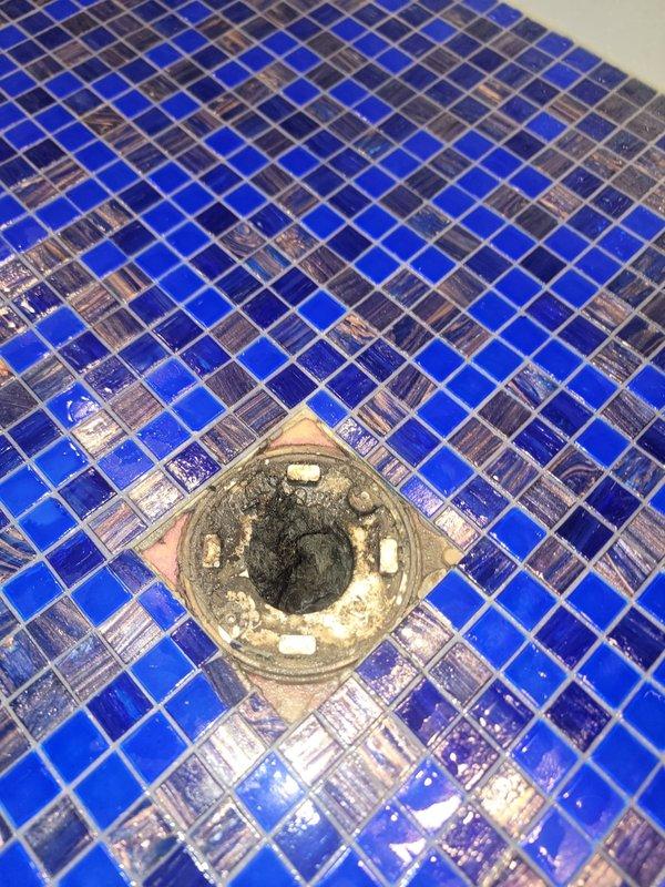 Responded to service call for shower drain with slow drainage issue. Upon inspection, found significant accumulation of hair, soap residue, and organic debris obstructing the drain assembly. Removed drain cover from blue mosaic tile shower floor and extracted large clump of matted hair and lint buildup from drain trap. Cleared all visible debris and mineral deposits from drain fixture and surrounding area. Tested drainage flow after cleaning to confirm proper water evacuation and restored full drainage functionality.