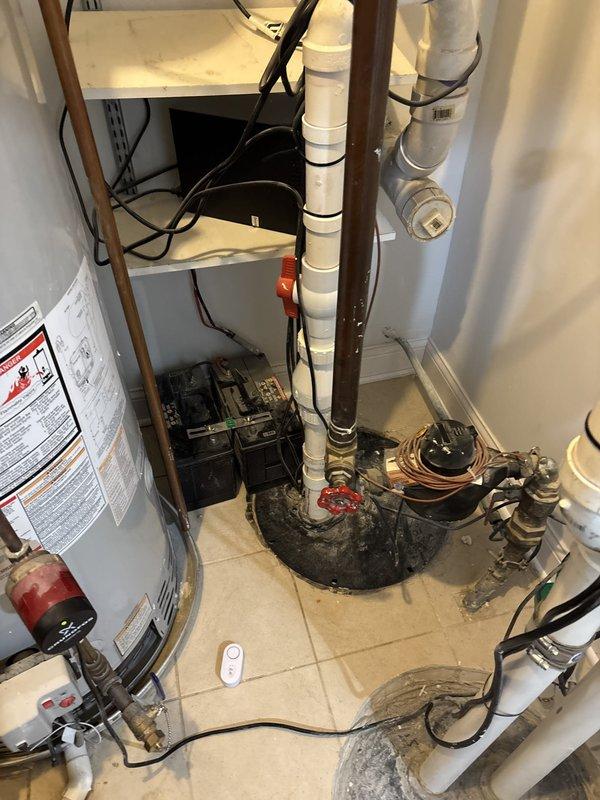 Responded to water leak in basement utility room following storm event. Upon inspection, identified active leak from pipe penetration through back wall near pump equipment, evidenced by vertical water marks on drywall and moisture accumulation on floor tiles. Traced leak source to compromised pipe collar at wall penetration point. Assessed surrounding plumbing infrastructure including water heater connections, PVC drainage lines, and copper supply lines for related damage. Documented moisture damage and leak location with photographic evidence showing water staining on utility room floor and wall penetration area. Recommended repair of pipe collar seal and monitoring of wall cavity for potential hidden moisture damage behind drywall.