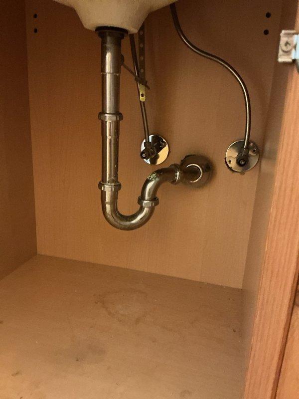 Responded to leaky faucet complaint in fifth-floor condo unit of thirteen-story residential high-rise. Upon inspection, assessed under-sink plumbing assembly including chrome P-trap, tailpiece, and supply lines with shut-off valves. Identified water damage and staining on cabinet floor indicating previous or ongoing leak. Tightened connections at drain assembly and supply line fittings, tested for leaks, and verified proper drainage function. Recommended monitoring cabinet area for additional moisture accumulation and potential replacement of deteriorated cabinet base materials if leaking persists.