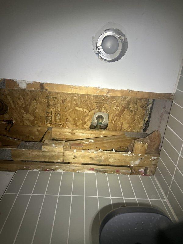 Responded to water leak complaint affecting downstairs area in 30-year-old residence. Conducted thorough leak inspection and traced source to bathroom plumbing system. Removed section of wall covering and drywall to access concealed piping behind bathtub enclosure, exposing structural framing and OSB sheathing. Located active leak in supply or drain lines servicing the tub/shower fixture assembly. Performed necessary repairs to compromised plumbing connections. Wall cavity left open for moisture monitoring and verification of repair effectiveness before reconstruction. Documented conditions with photos showing extent of access required and bathroom fixture configuration.
