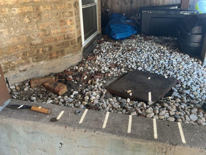 Responded to priority service call for failing catch basin in backyard of historic 130-year-old residence. Upon arrival, found circular catch basin with severely deteriorated concrete rim showing significant weathering, structural cracks, and brown/orange discoloration from prolonged moisture exposure and age. Basin contained standing water with sediment accumulation and debris, indicating compromised drainage function. The structure exhibited extensive surface deterioration around the circumference with the basin rim actively collapsing inward, creating a safety hazard in the landscaped area surrounded by river rock.

Assessed the structural integrity of the existing catch basin and determined complete replacement was necessary due to the advanced state of deterioration. Removed damaged concrete rim sections and deteriorated metal components visible in the work area. Excavated and cleared the basin opening, removing accumulated sediment, standing water, and organic debris from the vau