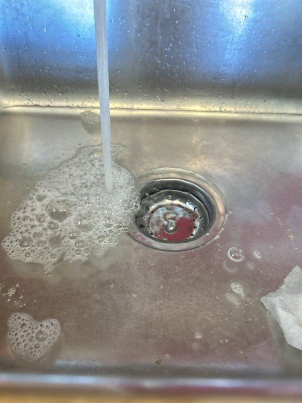 # Plumbing Service - Water Leak

Responded to a leaking kitchen sink in a 25-year-old residential property with original plumbing fixtures. Upon inspection, identified active water leak at the sink drain assembly beneath a stainless steel basin showing significant age-related wear and discoloration.

Accessed the cabinet interior and examined the chrome P-trap assembly and drain connections. Found water staining and moisture accumulation on the cabinet floor, indicating an ongoing leak from the drain system. The existing drain assembly consisted of a sink strainer, tailpiece extension, and U-shaped P-trap, all showing signs of deterioration consistent with the age of the plumbing system.

Inspected all visible supply lines, including flexible hoses and braided supply lines secured with metal fittings. Evaluated the integrity of all connections and seals throughout the drain assembly. Tested water flow to identify the exact source of the leak and assessed whether repair or replacement w