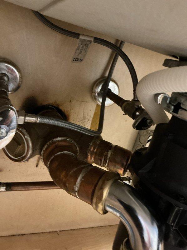 Responded to property inspection requirement for water heater system upgrade in highrise unit. Inspector identified undersized tankless water heater and inadequate supply piping that required upsizing to meet current code standards for property sale. Upon arrival, assessed existing plumbing infrastructure under sink areas, documenting corroded copper components and aging fixtures. Evaluated water supply line configuration, noting deteriorated piping with significant oxidation and patina buildup affecting flow capacity. Reviewed disposal connections, P-trap assembly, and flexible supply lines to determine compatibility with upgraded system requirements. Photographed existing conditions showing undersized piping, corroded copper fittings, and current water heater connections to support scope of work for tankless unit replacement and supply line upsizing necessary to satisfy inspection findings and facilitate property transaction.