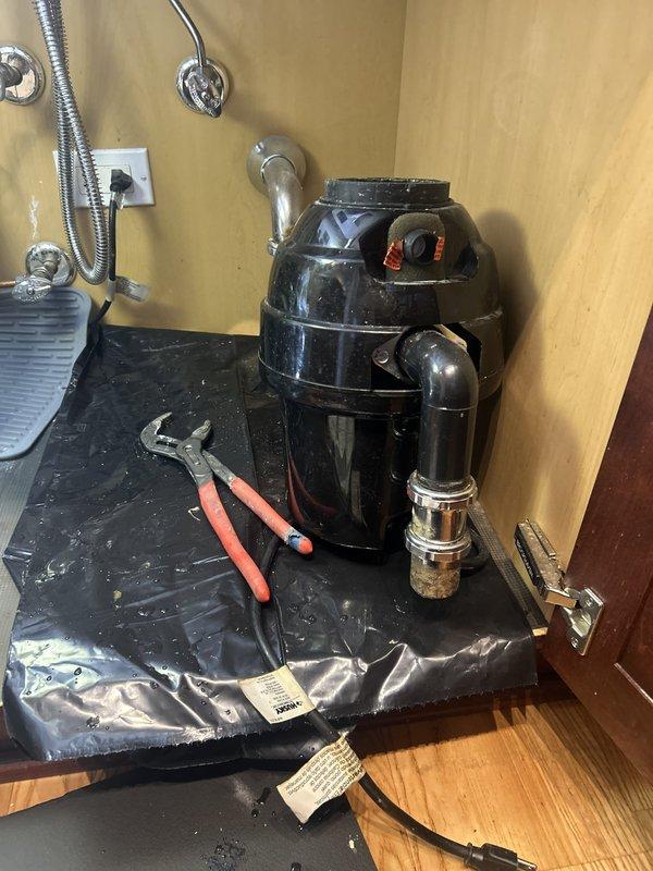 Responded to service call for garbage disposal replacement. Successfully removed existing disposal unit and installed new black cylindrical disposal unit under kitchen sink. Connected disposal to existing drain assembly with proper gasket seal and secured all chrome plumbing connections. Verified proper mounting, tested unit operation, and confirmed no leaks at drain or discharge connections. Protected work area with drop cloth and left installation clean and functional.