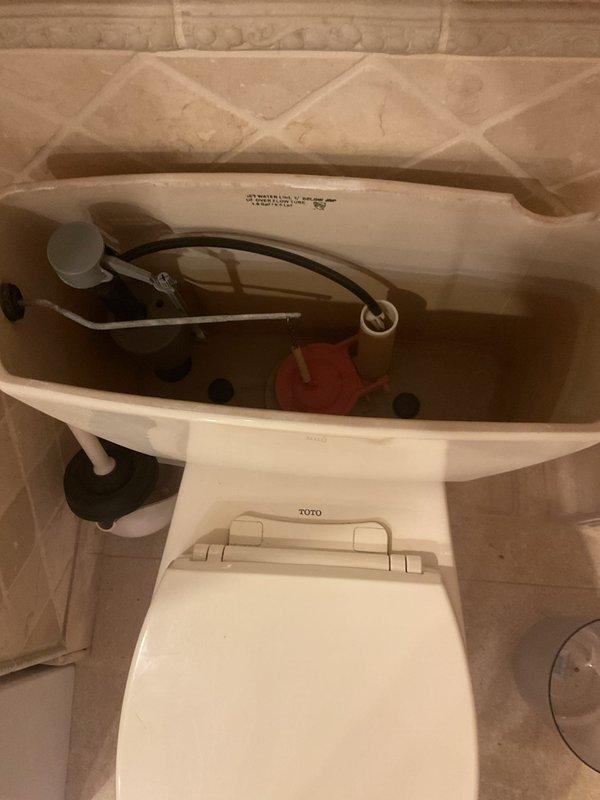 Responded to service call for TOTO toilet inspection and maintenance. Removed tank lid to assess internal flush mechanism components. Inspected flush valve assembly with red flapper seal, verified proper operation of fill valve and float mechanism, and checked for any signs of wear or leakage. All internal components found to be functioning within normal parameters. Tank interior examined for mineral buildup or deterioration. Reinstalled tank lid and confirmed toilet operational. Documented existing conditions with photographs for service records.