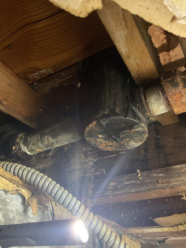Responded to clogged tub drain where customer's previous snake attempt resulted in a broken cable lodged in the line. Upon investigation, accessed crawl space beneath the fixture and discovered severely corroded cast iron drain piping with significant deterioration and oxidation throughout the assembly. The aging infrastructure showed extensive rust damage on the horizontal drain line and elbow joint, indicating long-term moisture exposure and structural compromise. Removed lodged snake cable from the deteriorated piping and assessed the overall condition of the drain system, documenting the corroded pipe assembly and surrounding wooden structural elements for future replacement recommendations.