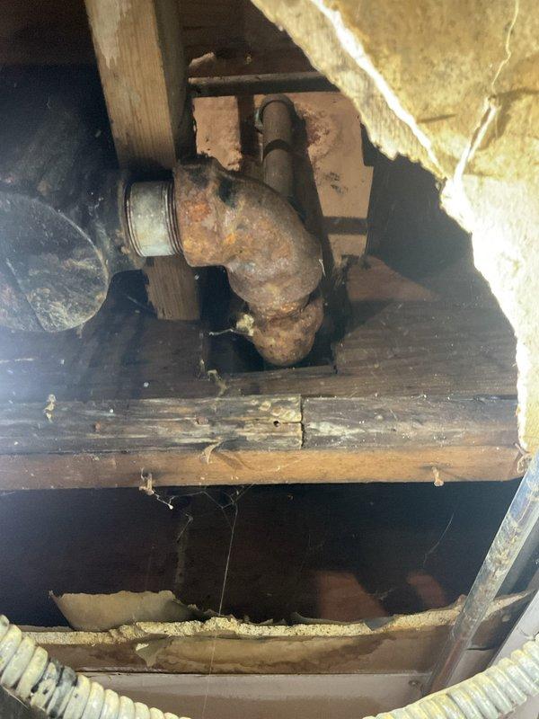Responded to clogged tub drain where customer's previous snake attempt resulted in a broken cable lodged in the line. Upon investigation, accessed crawl space beneath the fixture and discovered severely corroded cast iron drain piping with significant deterioration and oxidation throughout the assembly. The aging infrastructure showed extensive rust damage on the horizontal drain line and elbow joint, indicating long-term moisture exposure and structural compromise. Removed lodged snake cable from the deteriorated piping and assessed the overall condition of the drain system, documenting the corroded pipe assembly and surrounding wooden structural elements for future replacement recommendations.