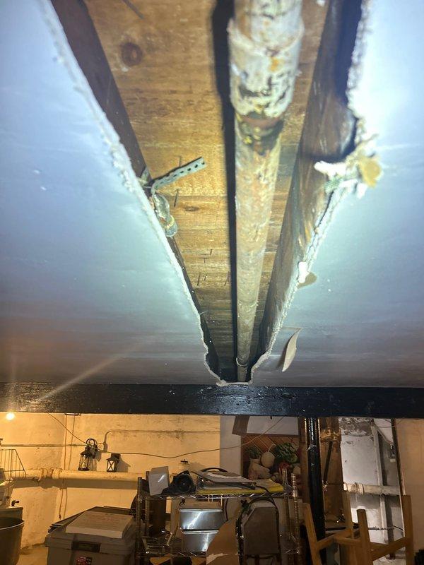 Completed installation of PVC piping junction in basement crawl space, including vertical riser and horizontal run with T-fitting connections. Addressed existing corrosion and rust staining around pipe fittings and joints, ensuring proper alignment through floor joists and structural openings. Documentation photos captured for quality assurance and future reference.