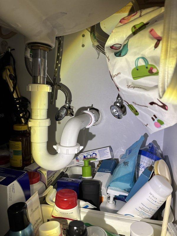 Responded to service call for two leaky Moen faucets in master bathroom and powder room. Inspected under-sink plumbing in both locations, examining P-trap assemblies, supply lines, and shut-off valves for proper installation and potential leak sources. Photographed existing plumbing configuration showing white PVC drain assemblies with some discoloration, flexible braided supply lines, and chrome shut-off valves. Also evaluated laundry area for reported sewer odor issues occurring during heavy rainfall, likely related to drain trap seal failure or venting problems that require further diagnostic assessment.