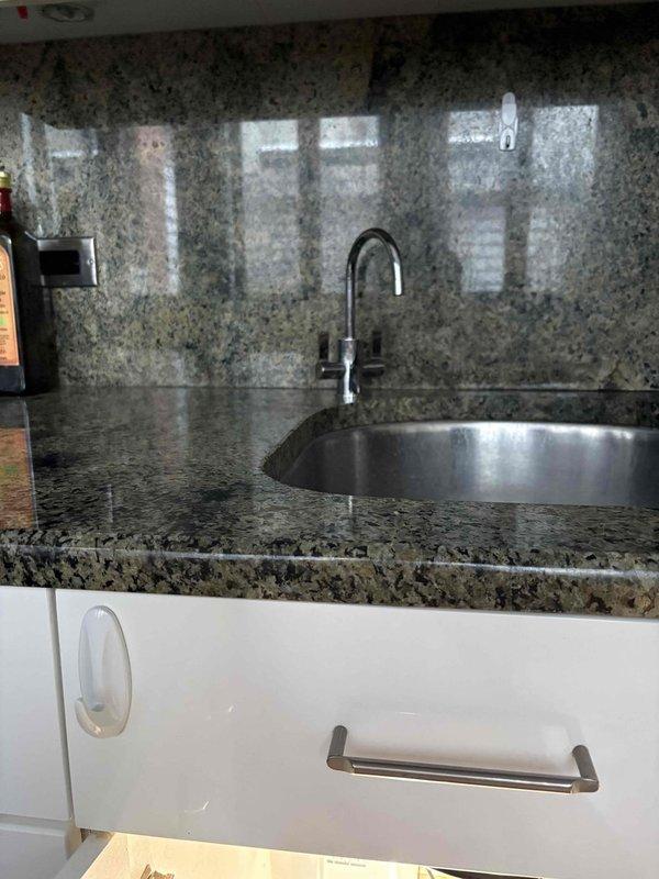 Installed tankless water filtration system under kitchen sink with undermount stainless steel basin and brushed metal single-handle faucet. Mounted TCM-WH electronic control unit to interior cabinet wall with three LED indicators and control buttons, integrated system with existing white PVC P-trap drain configuration and garbage disposal unit. Connected blue supply lines, electrical wiring, and plumbing connections to complete installation on granite countertop with matching backsplash and white gloss cabinetry.