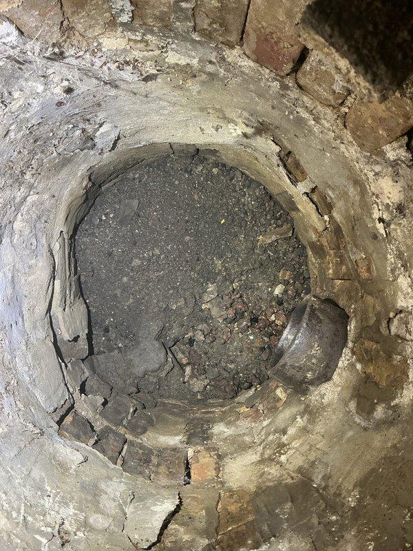 Conducted comprehensive assessment of existing water service infrastructure in basement area to determine requirements for water meter installation or complete water service line replacement. Documented current conditions including deteriorated concrete floor opening approximately 2-3 feet in diameter with significant cracking around perimeter where existing service line enters structure. Evaluated basement space showing aged concrete walls with deteriorating surfaces and exposed ceiling joists, noting existing plumbing infrastructure and utility connections. Photographed water service entry point and surrounding structural conditions to support preparation of detailed proposal. Assessment indicates potential need for permit, design, and plan (PDP) submission depending on scope of work selected by property owner for either meter installation at existing service line or full service line replacement from main to structure.