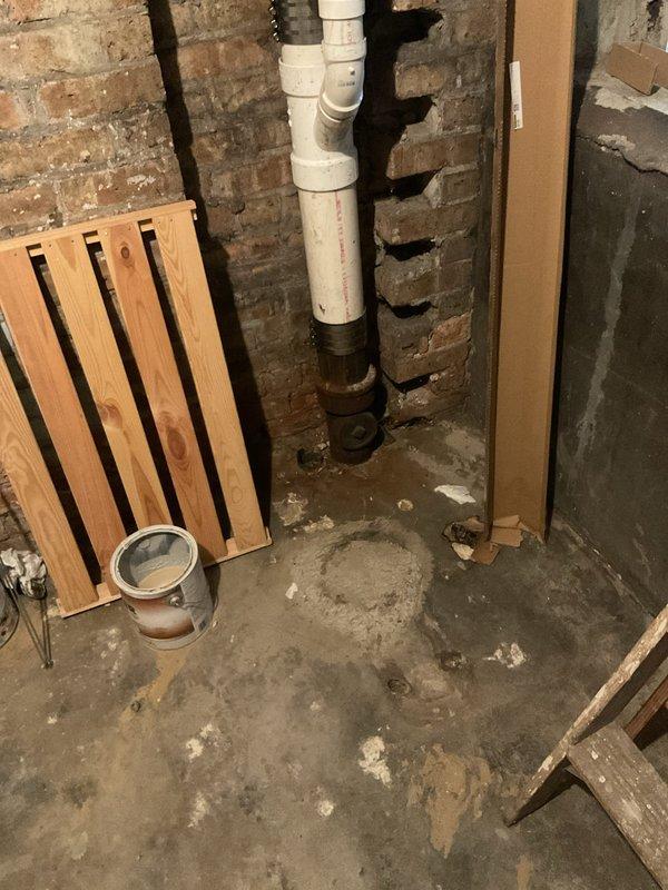 Responded to emergency plumbing call for failed ejector pump system in century-old residential property. Upon arrival, identified uncapped discharge pipe in basement as active source of water release, which had previously caused flooding. Inspected recently installed ejector pump (2024) and associated plumbing infrastructure, including vertical PVC discharge piping with multiple connection joints and coupling assembly. Documented existing conditions showing exposed brick foundation walls, concrete floor with evidence of prior water damage and staining, and compromised drainage system. Assessed structural elements of basement utility area and photographed failed pump installation, uncapped pipe terminus, and floor drain assembly to document extent of water damage and system failure. Provided technical evaluation of pump malfunction and recommended corrective action plan to address immediate water discharge issue and prevent future flooding events.