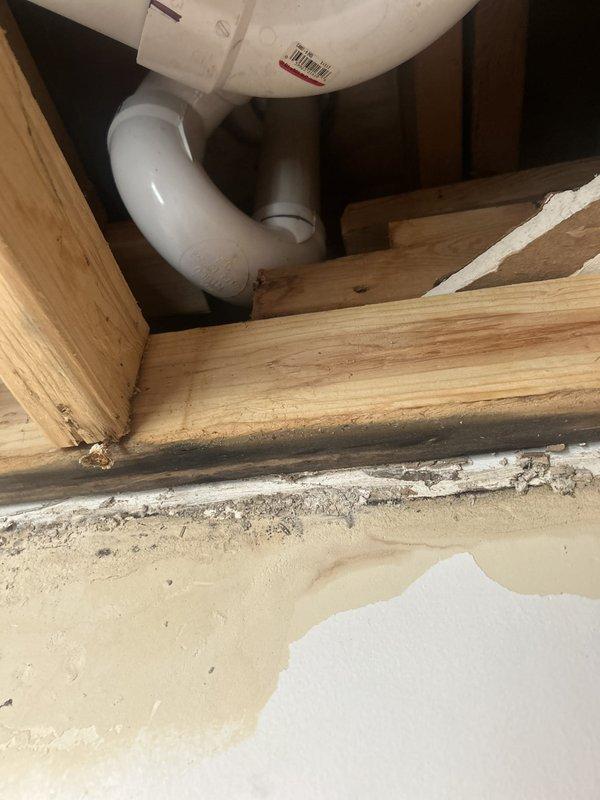 Responded to water leak originating from second-floor bathroom. Upon investigation, identified active leak in PVC drain assembly beneath bathroom fixtures causing water infiltration into floor cavity and migrating to first-floor kitchen cabinet below. Inspection revealed significant water staining and moisture damage on wooden floor framing members and cabinet interior surfaces, with visible discoloration and debris accumulation indicating prolonged exposure. Accessed affected areas through floor opening and under-sink cabinet to assess extent of damage. Documented conditions with photographs showing compromised PVC pipe connections, water-damaged framing, and saturated cabinet base for insurance documentation purposes. Provided detailed estimate outlining necessary repairs to plumbing system and water-damaged structural components.