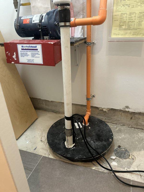Completed diagnostic assessment of non-operational sump pump system in basement utility area. The existing sump pump, less than ten years old, was evaluated for mechanical failure. System includes circular basin with black cover, white PVC discharge piping, red Steele-Grimell mounting bracket with associated motor unit, and orange PVC piping secured to wall with proper brackets. Electrical connections and pump functionality were inspected to determine cause of failure and provide repair or replacement recommendations. Additionally, successfully installed customer-supplied toilet fixture in bathroom, positioning one-piece elongated bowl unit on wood laminate flooring with proper mounting and connection to existing waste line. Faucet installation service was also completed per customer request using customer-provided fixtures. All installations were photographed for documentation purposes.