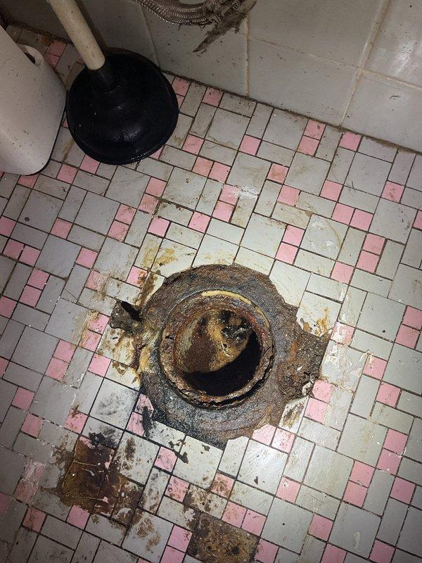 Responded to report of toilet leaking at base. Upon inspection, discovered significant corrosion and rust buildup on floor drain fixture adjacent to toilet, with deterioration extending to surrounding grout and tile surfaces. Removed toilet to access and assess leak source at base seal. Replaced wax ring and toilet mounting bolts. Inspected toilet flange for damage and verified proper seating. Reinstalled toilet, ensuring proper alignment and secure mounting to prevent future leaks. Tested for leaks by flushing multiple times and confirmed no water discharge at base. Advised regarding corroded floor drain fixture requiring future attention to prevent further deterioration of bathroom flooring.