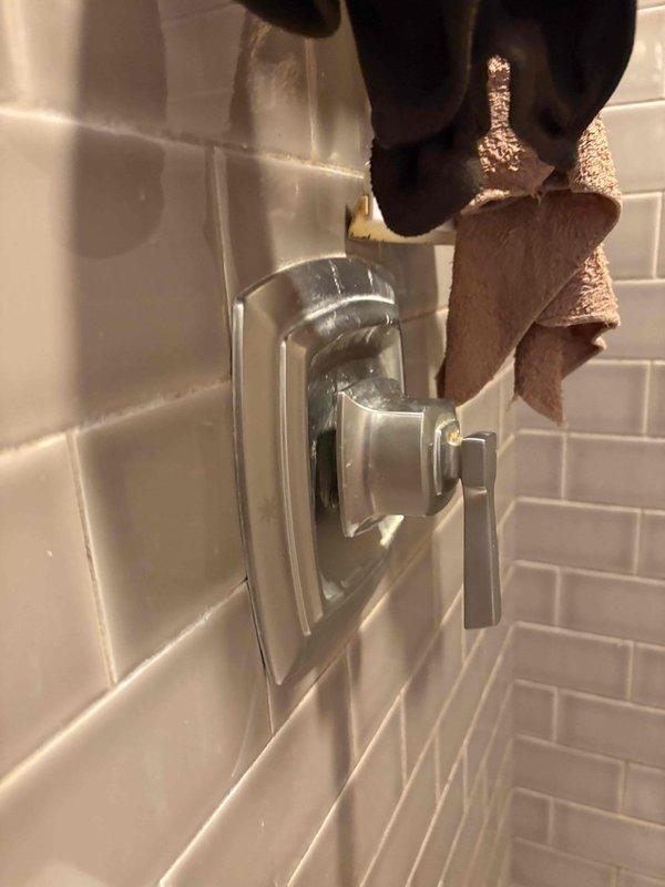 Conducted comprehensive plumbing assessment of residential piping system, documenting existing infrastructure in basement utility area and bathroom shower installation. Inspected exposed dark metal piping runs along basement wall, evaluating shut-off valve functionality and joint connections for proper operation. Assessed shower fixture installation featuring chrome recessed valve body with control lever, verifying proper mounting within white subway tile surround and documenting current system configuration for estimation purposes.