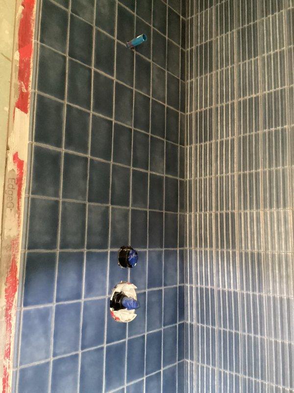 Completed shower trim installation in bathroom with blue ceramic tile walls. Installed shower valve control mechanism and shower arm connection, ensuring proper mounting and waterproofing integration with existing red membrane system. Provided estimate for vanity installation as requested.