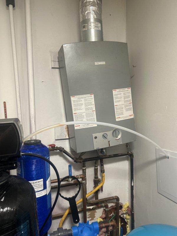 Responded to service call for malfunctioning water filtration and softening system at non-owner occupied property. Upon arrival, inspected comprehensive water treatment setup including Aquasure water softener with brine tank, multiple cylindrical filter housings with blue cartridge holders, and associated plumbing connections. Evaluated tankless water heater integration with treatment system, examining copper and PVC piping configurations, valve operations, and electrical control panel functionality. Diagnosed system performance issues, verified proper flow through filter housings and softener tank, checked brine tank levels and settings on digital control display. Restored water treatment system to proper working condition and documented installation with photographs for service records.