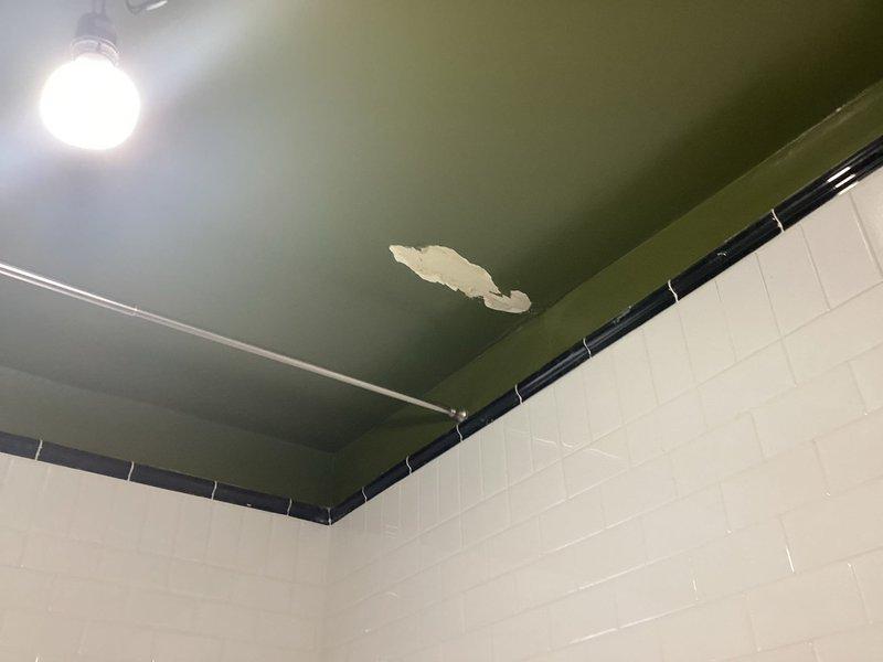 Responded to service call for ceiling water damage in bathroom. Upon inspection, discovered significant paint peeling on ceiling caused by active plumbing leak from above. Opened ceiling access point to expose source of water intrusion. Located compromised supply line running through wall cavity between floor joists. Removed section of ceiling material and exposed framing to access piping. Repaired leaking pipe connection and secured all plumbing fixtures. Documented existing conditions showing water-damaged ceiling paint, exposed wall framing, and piping configuration for insurance and restoration purposes.
