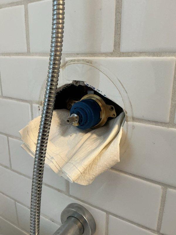 Diagnosed faulty shower cartridge in bathroom tub/shower combination requiring replacement. Accessed valve assembly through existing wall opening in white subway tile surround and confirmed cartridge failure with blue plastic components visible on brass valve body. Coordinated with building management to schedule water shutdown for complete cartridge replacement, as building plumbing system requires main water supply isolation to perform repair safely and prevent water damage to unit and adjacent spaces.