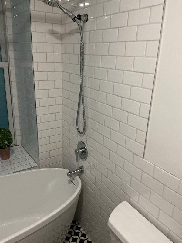 Diagnosed faulty shower cartridge in bathroom tub/shower combination requiring replacement. Accessed valve assembly through existing wall opening in white subway tile surround and confirmed cartridge failure with blue plastic components visible on brass valve body. Coordinated with building management to schedule water shutdown for complete cartridge replacement, as building plumbing system requires main water supply isolation to perform repair safely and prevent water damage to unit and adjacent spaces.