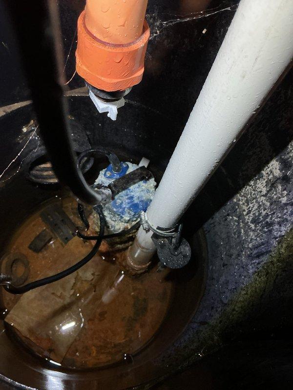 Responded to emergency flood control call for basement water intrusion detected by water sensor. Upon arrival, inspected sump pump system and found active water accumulation in sump pit with functioning pump assembly. Documented existing installation consisting of submersible sump pump with PVC discharge piping, check valve, and electrical connections. System assessed and verified operational status to prevent further flooding.