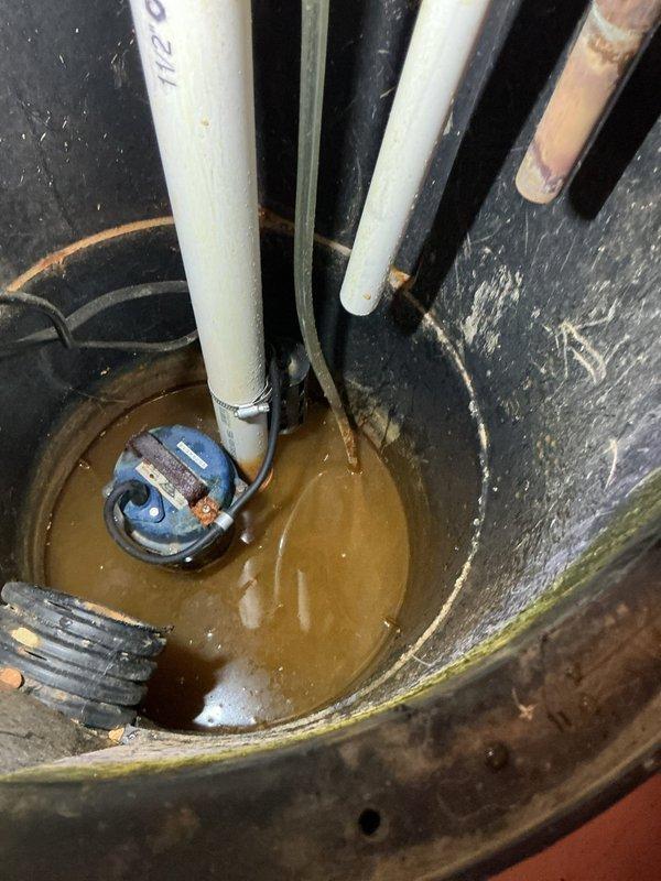 Responded to emergency flood control call for basement water intrusion detected by water sensor. Upon arrival, inspected sump pump system and found active water accumulation in sump pit with functioning pump assembly. Documented existing installation consisting of submersible sump pump with PVC discharge piping, check valve, and electrical connections. System assessed and verified operational status to prevent further flooding.
