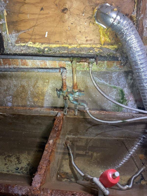 Responded to a broken pipe issue in the basement of a century-old home. Upon inspection, discovered severely corroded galvanized plumbing with advanced deterioration, including two old shutoff valves exhibiting heavy turquoise and orange oxidation, and vertical supply pipes with extensive rust degradation. The affected area showed significant water damage to surrounding wooden structural elements, with biological growth and moisture staining throughout the crawl space. The deteriorated piping system, while currently draining to a sink without active leaking, poses imminent failure risk due to advanced corrosion. Documented the condition with photographs showing compromised valve assemblies, rusted horizontal and vertical runs, and additional corroded components scattered on the concrete floor. Provided estimate for complete pipe replacement of the affected sections, recommending modern piping materials suitable for the existing infrastructure of this older residential property.