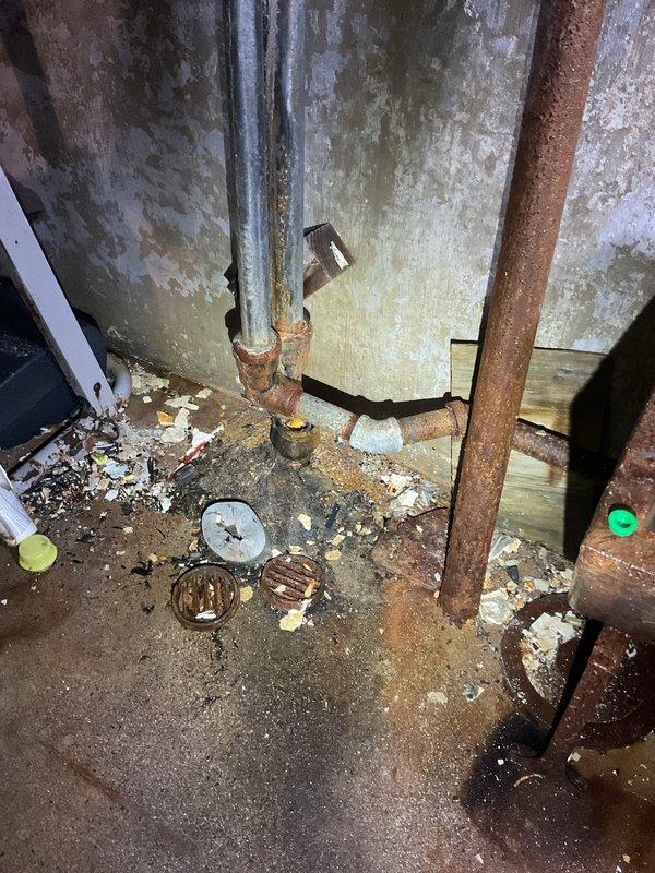 Responded to a broken pipe issue in the basement of a century-old home. Upon inspection, discovered severely corroded galvanized plumbing with advanced deterioration, including two old shutoff valves exhibiting heavy turquoise and orange oxidation, and vertical supply pipes with extensive rust degradation. The affected area showed significant water damage to surrounding wooden structural elements, with biological growth and moisture staining throughout the crawl space. The deteriorated piping system, while currently draining to a sink without active leaking, poses imminent failure risk due to advanced corrosion. Documented the condition with photographs showing compromised valve assemblies, rusted horizontal and vertical runs, and additional corroded components scattered on the concrete floor. Provided estimate for complete pipe replacement of the affected sections, recommending modern piping materials suitable for the existing infrastructure of this older residential property.