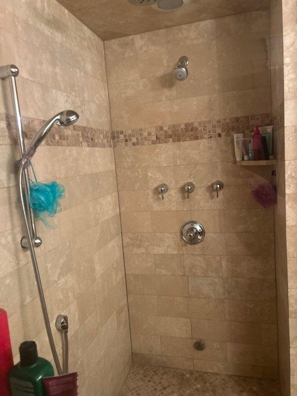 Responded to service call for shower with no cold water supply. Inspected existing shower system with multiple chrome control valves and handheld showerhead on slide bar. Diagnosed temperature control issue affecting cold water delivery to fixtures. Documented existing tile shower enclosure with travertine-style tile walls, mosaic border detail, and dual showerhead configuration. Provided estimate for steam shower installation as requested.