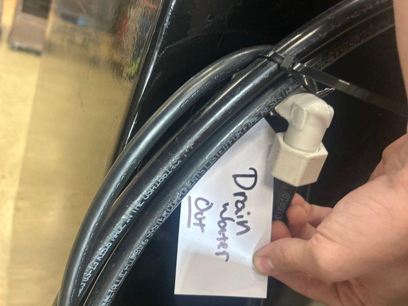 Completed installation of valve on water supply line and connected drainage system for new plumbing fixture. Installed blue expansion tank with copper piping connections, routed black flexible drain tubing, and integrated control unit with digital display panel for system monitoring and operation.
