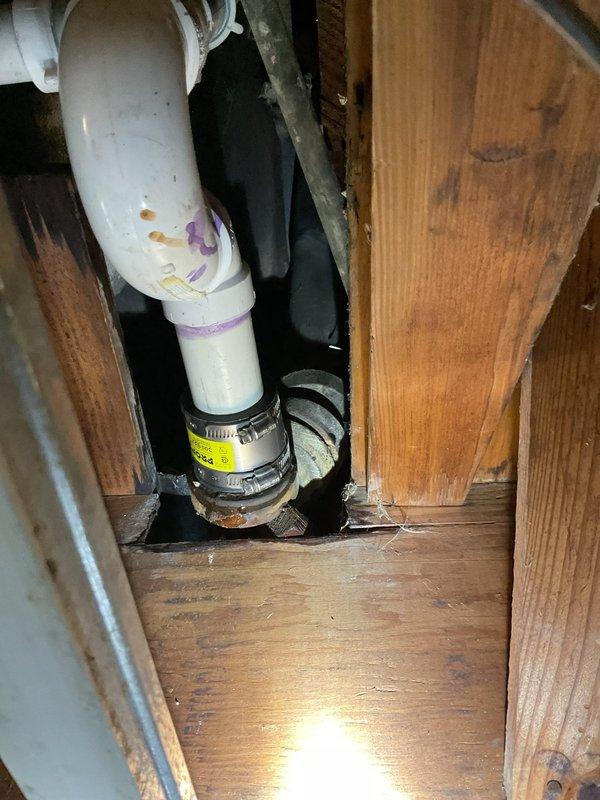 Responded to active water leak dripping into basement ceiling in 85-year-old residence. Upon inspection, identified deteriorated plumbing connections at brass cross-valve manifold with aged copper piping showing significant corrosion and tarnishing. Water staining on surrounding wall indicated ongoing moisture intrusion from compromised fittings. Accessed plumbing system through cabinet area beneath structure. Replaced failed connections using PVC pipe with proper primer application and secured flexible coupling with metal hose clamp to ensure watertight seal. Repaired vertical chrome pipe section with new blue plastic connectors at joints. Addressed single affected area and verified all connections for proper flow and eliminated active leak. System tested and confirmed operational with no further water intrusion detected.