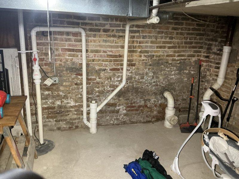 Conducted site assessment of basement catch basin system to provide estimate for sealing existing catch basin and connecting drainage to municipal sewer line. Documented current plumbing configuration including exposed PVC drainage piping, existing catch basin location, and basement conditions showing historical moisture infiltration evidenced by efflorescence on brick walls, which supports the need for proper drainage connection to city system.