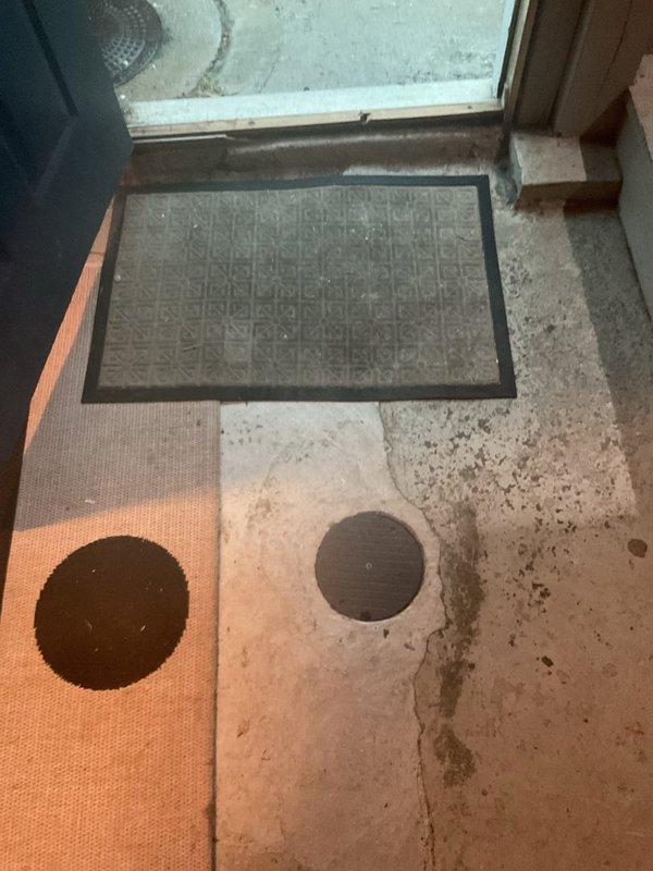 Conducted comprehensive inspection of catch basin and downspout system at 133-year-old residential property to assess condition and identify potential repair or replacement needs. Utilized camera equipment to snake through downspouts and thoroughly inspect cleanout access points. Documented exterior catch basin cover showing rust and weathering, interior cleanout access points in concrete flooring near entry threshold, and secondary drainage grate system. All accessible components were visually inspected and photographed for assessment purposes.