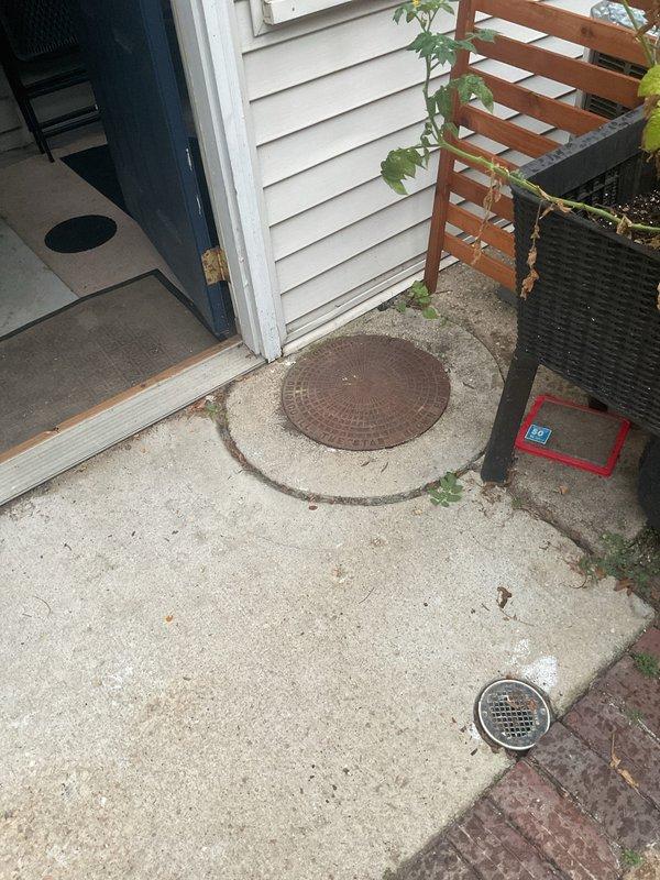 Conducted comprehensive inspection of catch basin and downspout system at 133-year-old residential property to assess condition and identify potential repair or replacement needs. Utilized camera equipment to snake through downspouts and thoroughly inspect cleanout access points. Documented exterior catch basin cover showing rust and weathering, interior cleanout access points in concrete flooring near entry threshold, and secondary drainage grate system. All accessible components were visually inspected and photographed for assessment purposes.