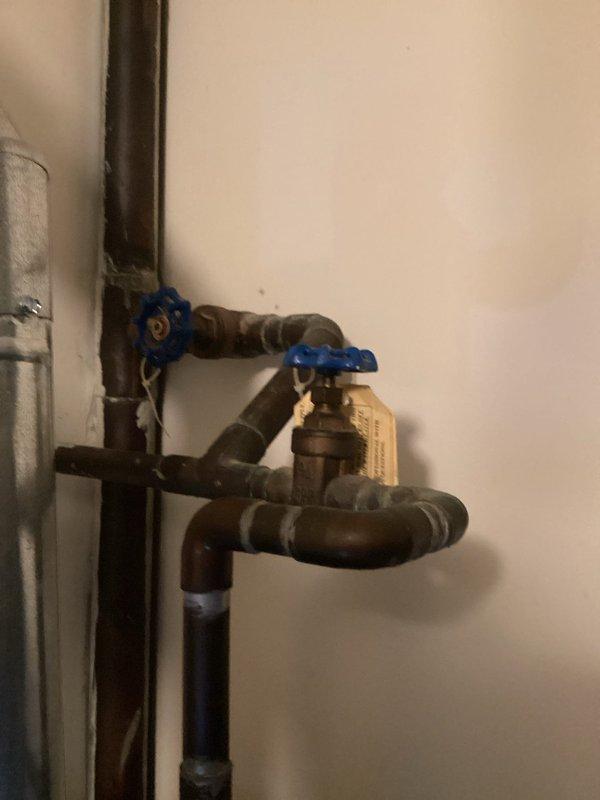Responded to service call for plumbing system evaluation. Inspected aged brass/copper multi-valve assembly showing significant corrosion and oxidation, with two blue-handled shut-off valves requiring assessment. Documented existing plumbing configuration and condition of fixtures in residential bathroom for repair recommendation and future service planning.