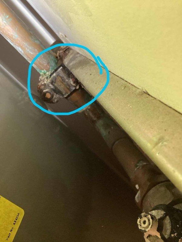 Responded to water leak complaint near tank area. Upon inspection, located active leak on vertical copper supply line and identified significant corrosion at pipe junction point with mounting bracket. Documented corroded connections displaying greenish-blue patina and rust-colored staining, indicating prolonged moisture exposure and deterioration of plumbing infrastructure.