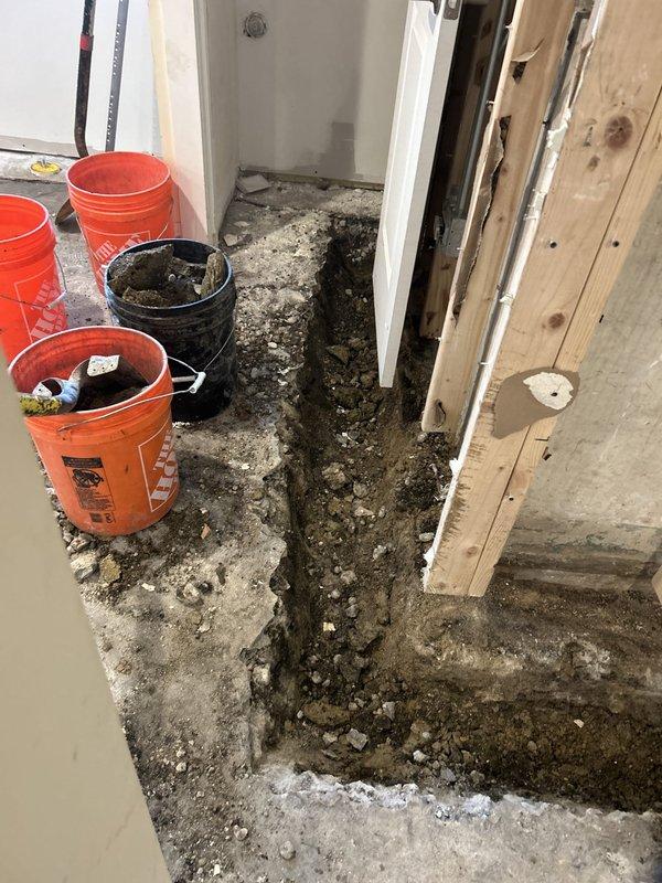 Responded to site for drain tile inspection and assessment. Upon arrival, found significant water damage and deterioration to interior concrete floor with extensive dark staining and sediment accumulation throughout the affected area. Documented existing conditions showing severe floor degradation with visible channel or depression filled with contaminated material running through center of space. Observed exposed wall framing indicating previous water intrusion issues. Inspected white corrugated drainage pipe installation at floor level near doorway threshold. Pipe appeared to be functioning as part of interior perimeter drain tile system. Assessed concrete condition around pipe penetration point, noting rough edges and exposed aggregate consistent with recent excavation or repair work. Photographed all affected areas including deteriorated flooring, sediment deposits, wall damage, and drainage pipe configuration for documentation and future reference. Work area showed signs of ongoin