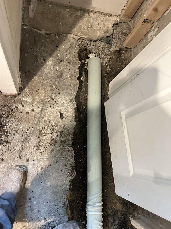 Responded to site for drain tile inspection and assessment. Upon arrival, found significant water damage and deterioration to interior concrete floor with extensive dark staining and sediment accumulation throughout the affected area. Documented existing conditions showing severe floor degradation with visible channel or depression filled with contaminated material running through center of space. Observed exposed wall framing indicating previous water intrusion issues. Inspected white corrugated drainage pipe installation at floor level near doorway threshold. Pipe appeared to be functioning as part of interior perimeter drain tile system. Assessed concrete condition around pipe penetration point, noting rough edges and exposed aggregate consistent with recent excavation or repair work. Photographed all affected areas including deteriorated flooring, sediment deposits, wall damage, and drainage pipe configuration for documentation and future reference. Work area showed signs of ongoin