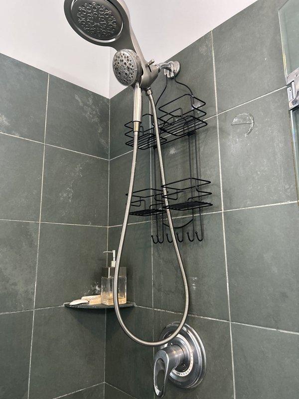 Completed shower valve repair and inspection of dual showerhead system. Serviced Gerber brand shower control valve, ensuring proper operation of temperature control mechanism and verified OFF position functionality. Inspected chrome fixtures, handheld showerhead assembly with sliding bar bracket, and overhead rain showerhead for proper water flow and secure mounting on tiled shower enclosure.
