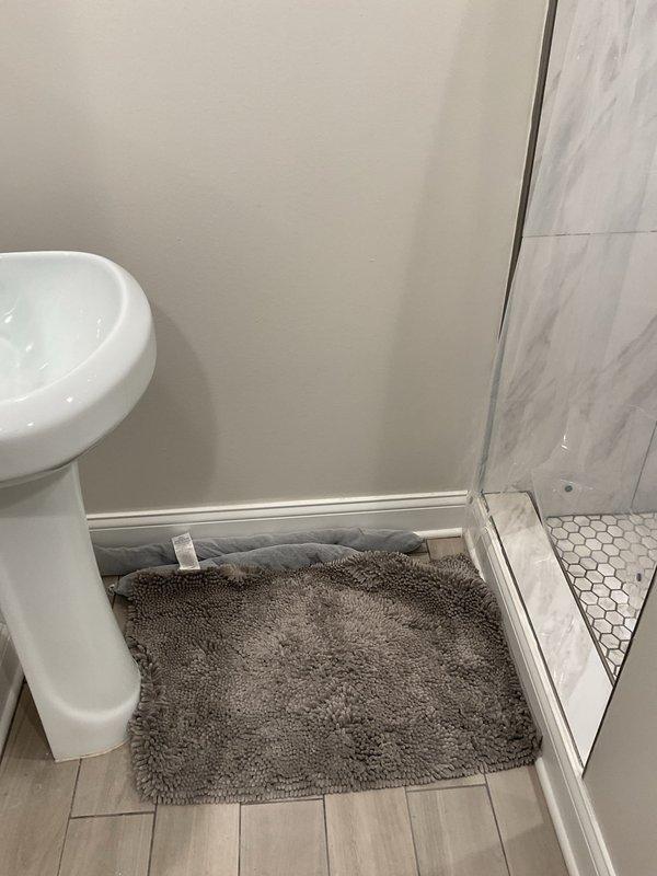 Responded to basement flooding complaint and conducted comprehensive inspection of plumbing system and bathroom facilities. Evaluated white PVC drainage piping configuration in utility area, examining vertical and horizontal runs, connections, and joints for potential failure points or blockages that could contribute to water backup. Inspected bathroom with wood-grain tile flooring and modern fixtures, assessing shower drain system with hexagonal tile base and glass enclosure for proper drainage function. Documented existing plumbing infrastructure including exposed pipe routing, mineral deposit accumulation on vertical lines, and proximity to HVAC ductwork components. Verified proper installation of drainage system connections and assessed potential sources of water intrusion affecting basement area.