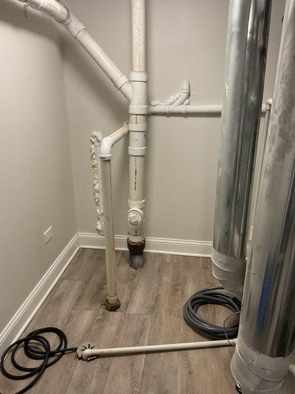 Responded to basement flooding complaint and conducted comprehensive inspection of plumbing system and bathroom facilities. Evaluated white PVC drainage piping configuration in utility area, examining vertical and horizontal runs, connections, and joints for potential failure points or blockages that could contribute to water backup. Inspected bathroom with wood-grain tile flooring and modern fixtures, assessing shower drain system with hexagonal tile base and glass enclosure for proper drainage function. Documented existing plumbing infrastructure including exposed pipe routing, mineral deposit accumulation on vertical lines, and proximity to HVAC ductwork components. Verified proper installation of drainage system connections and assessed potential sources of water intrusion affecting basement area.