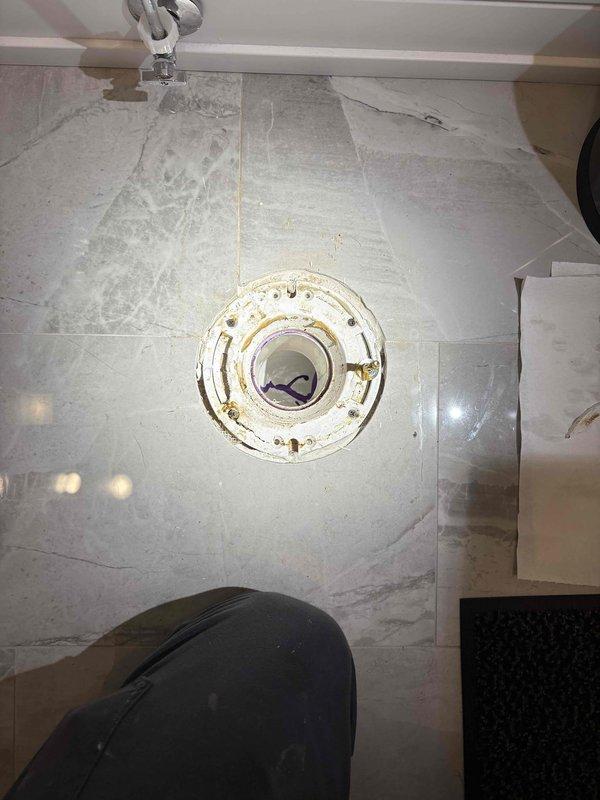Conducted VIP plumbing maintenance inspection of bathroom floor drain assembly. Documented existing drain fixture showing significant age-related deterioration, rust staining around mounting fasteners, and corroded white circular flange with protective yellow Oatey cap in place. Assessment determined that specialized equipment is required to complete necessary repairs. Scheduled follow-up visit with tall ladder and additional technician to properly access and service the drain system.