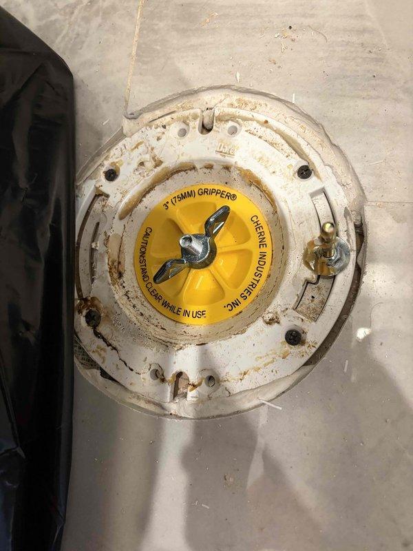 Conducted VIP plumbing maintenance inspection of bathroom floor drain assembly. Documented existing drain fixture showing significant age-related deterioration, rust staining around mounting fasteners, and corroded white circular flange with protective yellow Oatey cap in place. Assessment determined that specialized equipment is required to complete necessary repairs. Scheduled follow-up visit with tall ladder and additional technician to properly access and service the drain system.