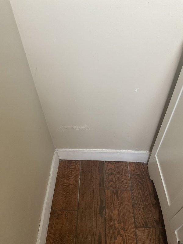 Responded to commercial water leak investigation behind interior wall. Upon inspection, discovered active moisture intrusion affecting under-sink cabinet area with visible water damage, discoloration, and potential mold growth along baseboards and corner joints. Examined PVC drain plumbing system and identified corrosion on metal pipe connections as probable leak source. Documented conditions with photographs showing extent of water damage to walls, flooring, and cabinet interior. Provided estimate for necessary repairs including wall access, pipe replacement, and water damage remediation.